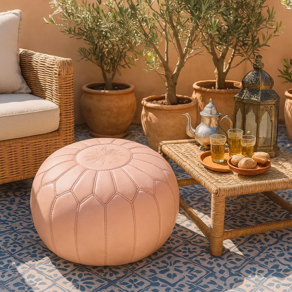 Pink pouf on a sunlit Moroccan patio with tea glasses, pastries, and woven decor, set against terracotta planters and tiled flooring.