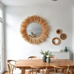 Suspended straw mirror with handwoven frame and natural linen rope above wooden dining table in minimalist boho space