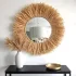 Close-up of handwoven straw hanging mirror showing natural raffia texture and rope suspension detail above black console