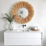 Handwoven straw suspended mirror with natural rope above white floating vanity in organic spa-inspired bathroom