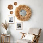 Handwoven hanging mirror with natural straw fringe displayed in gallery wall arrangement with art prints and natural decor