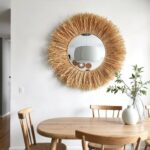Natural raffia hanging mirror with rope detail above round dining table creating warm farmhouse coastal aesthetic