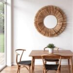 Handwoven raffia round mirror above modern dining table with chairs creating organic farmhouse wall art accent