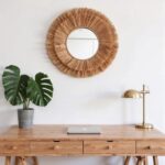 Natural straw round mirror above wooden dresser with monstera plant and brass lamp in minimalist boho bedroom