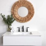 Natural raffia round mirror above white bathroom vanity sink creating spa-like organic wall decor in powder room