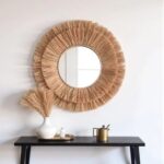 Handwoven round straw mirror hung above black console table with gold accents showing farmhouse wall decor styling