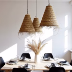 Trio of handmade straw lamps hanging above wooden dining table with black chairs