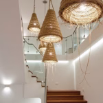Cascade of straw lamps in varying sizes illuminating modern staircase with glass railing