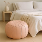 Soft pink pouf at the foot of a neatly made bed in a minimalist bedroom, paired with neutral bedding and light wood furniture.
