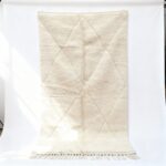 White Moroccan rug with diamond geometric pattern and fringe, handmade wool texture close-up view