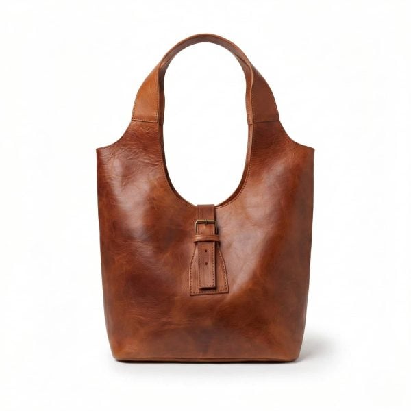 Studio shot of a minimalist brown leather shoulder bag isolated on a white background, featuring a curved hobo-style silhouette and a central vertical strap with a brass buckle.