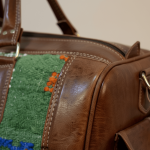 Close-up detail of kilim leather duffle bag showing green wool panel stitching, leather edge, and quality brass hardware