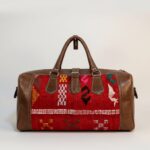 Kilim leather duffle bag with red handwoven wool panels and brown leather trim, featuring dual handles and brass hardware