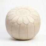 A handcrafted Moroccan undyed genuine leather pouf in a natural off-white tone, featuring traditional embroidery and vertical stitched panels.