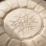 Extreme close-up of the artisanal embroidery on an undyed genuine leather pouf, highlighting the natural texture of the raw, untreated leather.