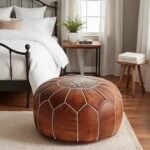 Tan leather floor ottoman with white embroidery on a textured rug in a minimalist neutral bedroom
