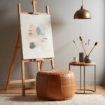 Handcrafted tan leather floor ottoman beside art easel in creative studio space with pendant light
