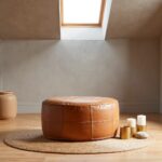 Tan leather floor ottoman in artist studio with canvas easel and paintbrushes warm lighting