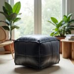 Black leather square pouf for floor seating near window with natural light and plants