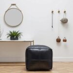 Black leather square pouf between beige accent chairs in contemporary living room with arc lamp