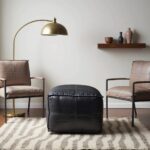 Black leather square pouf in modern entryway with round mirror and decorative wall hooks