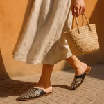 Street-style walk black Moroccan babouche slipper worn with flowing linen skirt and woven basket bag against warm adobe wall.