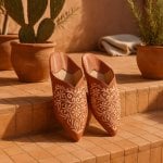Terracotta engraved leather babouche with gold floral arabesque embossing on sun-lit terracotta tiles with cacti