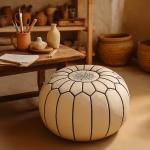 White leather pouf in an artisan studio setting beside a rustic wooden workbench and pottery tools.