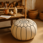 Handcrafted white leather floor ottoman with black geometric stitching in artisan studio with pottery backdrop