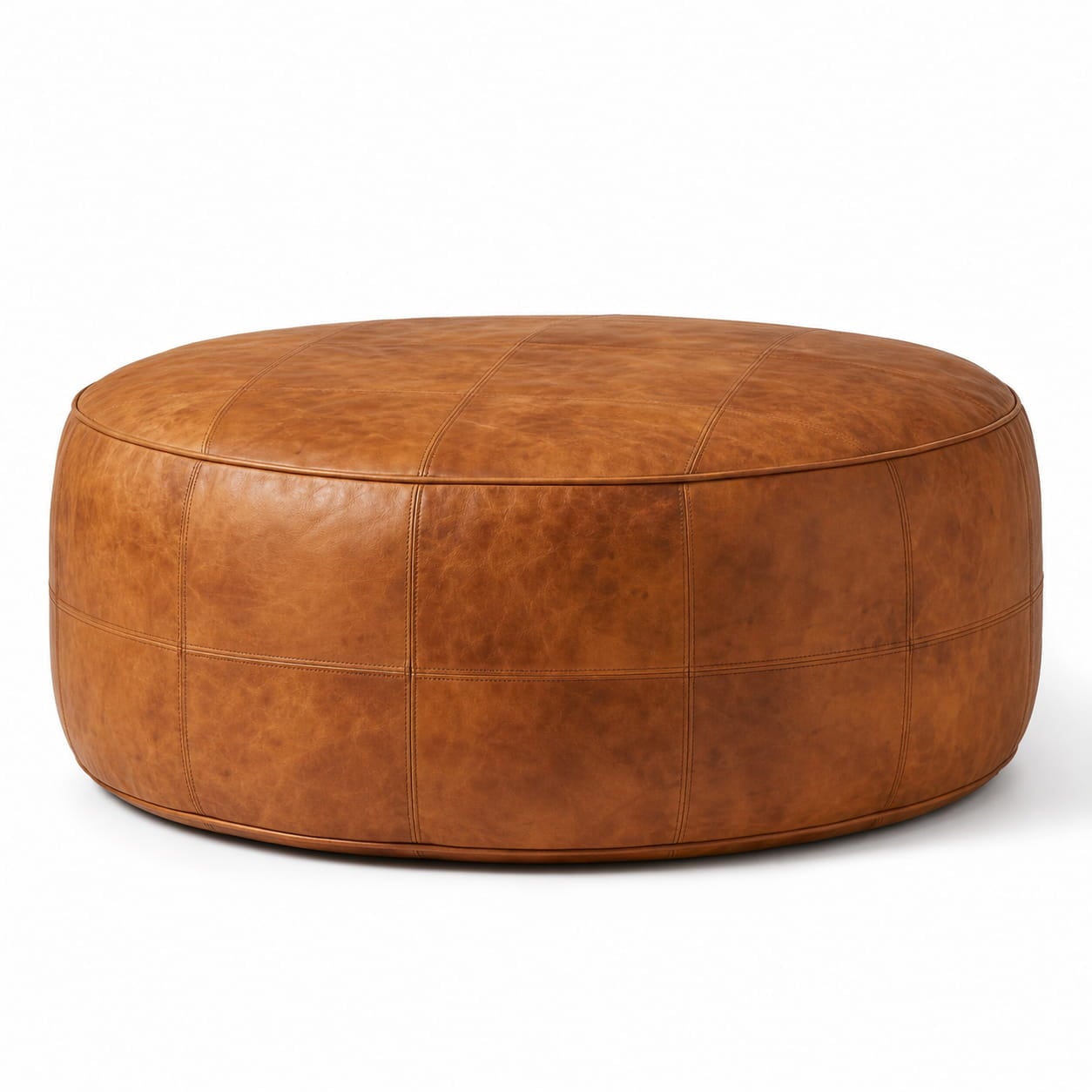round-tan-leather-floor-ottoman-white-background. A studio product shot of a round, stitched tan leather floor ottoman with a natural grain texture, isolated against a clean white background.
