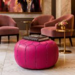 Pink leather round ottoman styled in modern living room with velvet chairs and Christian Dior book as coffee table