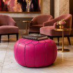 Pink leather round ottoman styled in modern living room with velvet chairs and Christian Dior book as coffee table