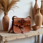 Brown leather shoulder bag styled on rustic wooden shelf with terracotta pottery and earth tones