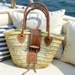 Leather straw tote resting on boat cushion with braided handles and wooden toggle