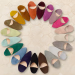 Circle arrangement of colorful suede Moroccan slippers in twenty vibrant shades on patterned tile floor, creating a rainbow wheel effect.