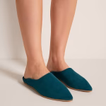 Close-up of teal Moroccan slippers on feet against neutral studio backdrop, showing sleek pointed toe and natural leather sole.