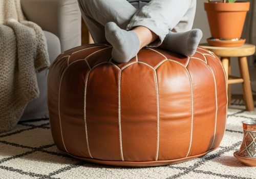 A beautiful, firm, and fully stuffed natural brown Moroccan leather pouf being used as a footrest in a sunlit, bohemian living room.