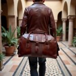 Man carrying brown leather travel bag for men with embossed panel in Spanish colonial courtyard