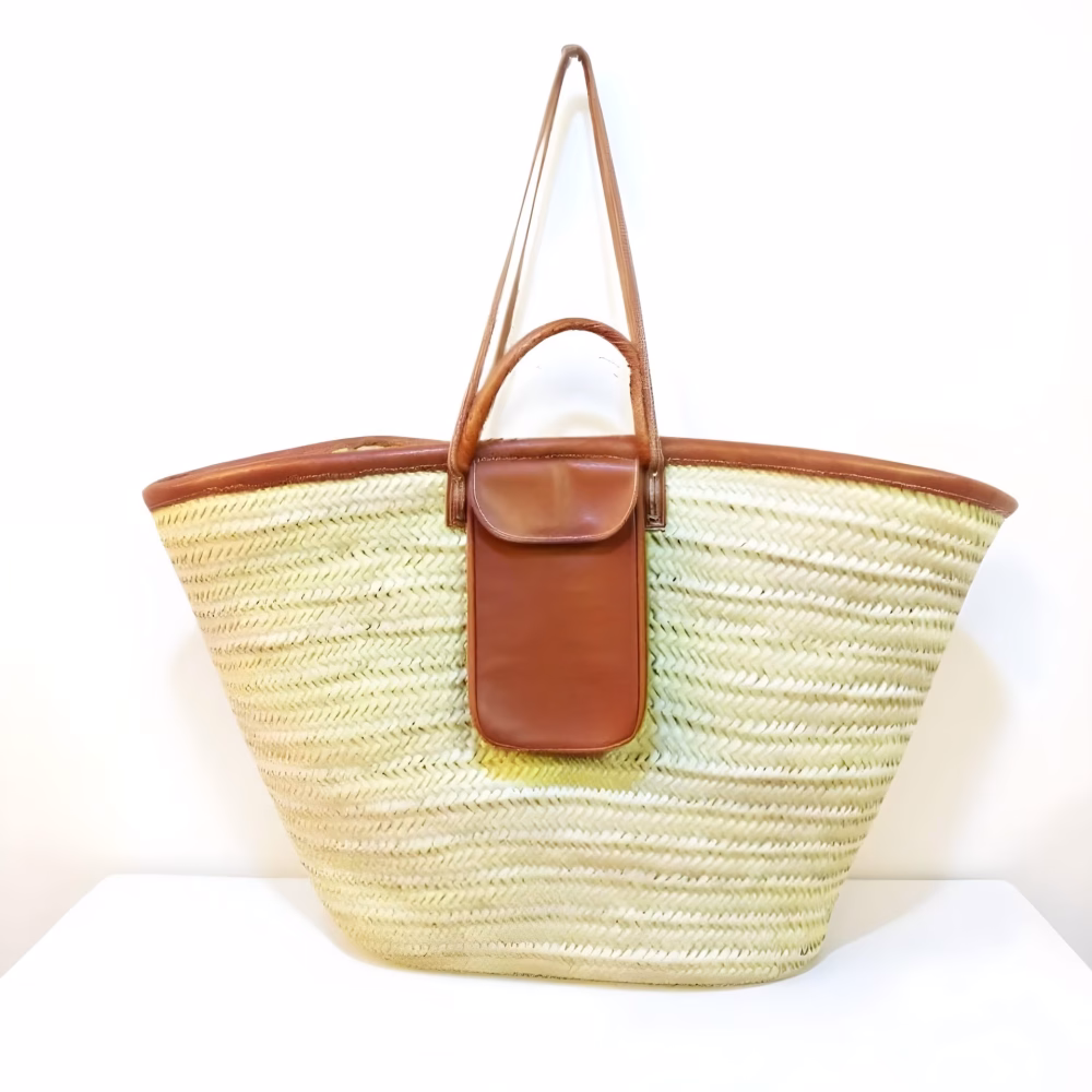 Natural straw beach bag with brown leather pocket and straps on white background