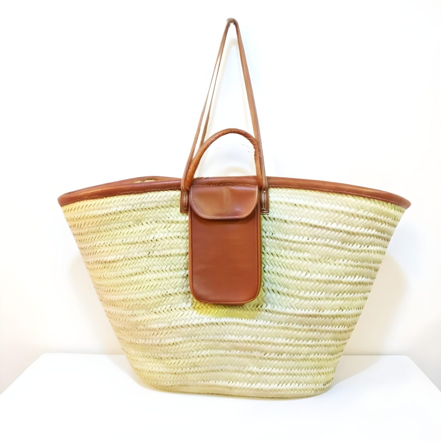 Moroccan straw handbag with outside pocket Natural straw beach bag with brown leather handles and front pocket on white background