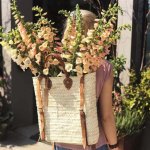 Straw backpack purse worn as convertible tote with flowers, brown leather handles, natural woven texture shown