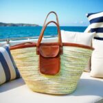 Straw shoulder bag with leather pocket and handles on boat deck overlooking blue ocean