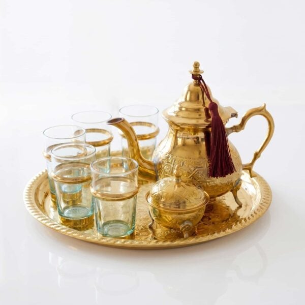Handcrafted brass tea set 9-piece with sugar bowl, featuring an engraved teapot with a burgundy tassel, six glasses with brass holders, and a matching serving tray isolated on a clean white background.