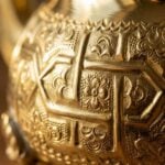 Extreme close-up of the intricate hand-engraved floral patterns and geometric textures on a teapot from a moroccan brass tea set.