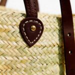 Macro close-up of hand-stitched teardrop leather mounting patch with brass rivet on natural palm straw chevron weave, artisan straw backpack purse