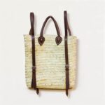 Handwoven straw backpack purse with dark brown leather shoulder straps and teardrop mounting patches, front view on white background