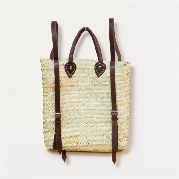 Handwoven straw backpack purse with dark brown leather shoulder straps and teardrop mounting patches, front view on white background