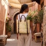 Woman wearing handwoven straw backpack purse with leather straps in a Moroccan medina alleyway, fresh flowers in open top