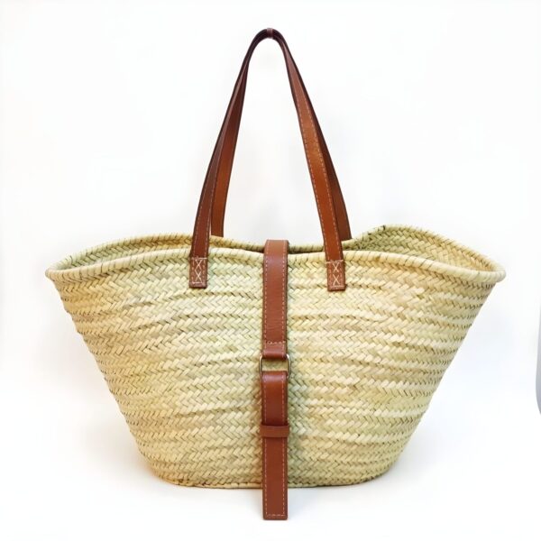 Handwoven palm leaf belted straw bag with brown leather straps and metal buckle on white background