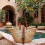 Belted straw bag with brown leather handles beside stone courtyard pool with orange tree